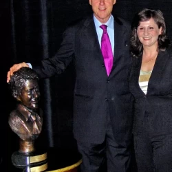 Bill Clinton standing next to a bronze bust of himself